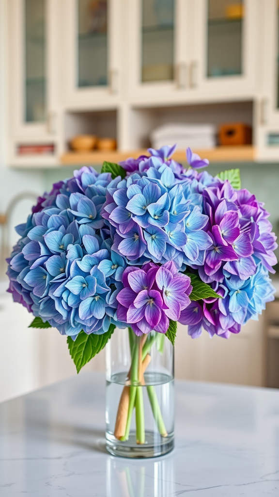 A bouquet of blue and purple hydrangeas in a clear vase on a kitchen counter.