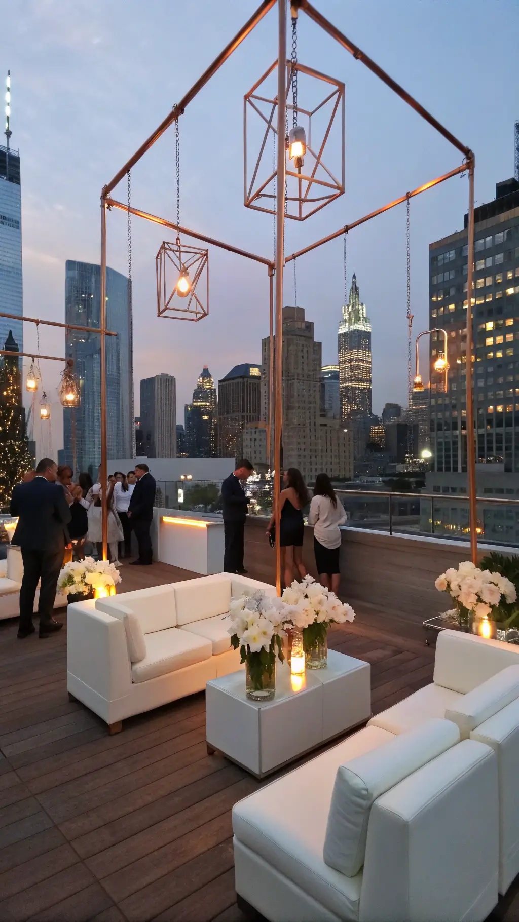 A stylish rooftop cocktail hour at blue hour with white leather furniture, lucite tables, and suspended copper frames adorned with white orchids, overlooking a twinkling city skyline.