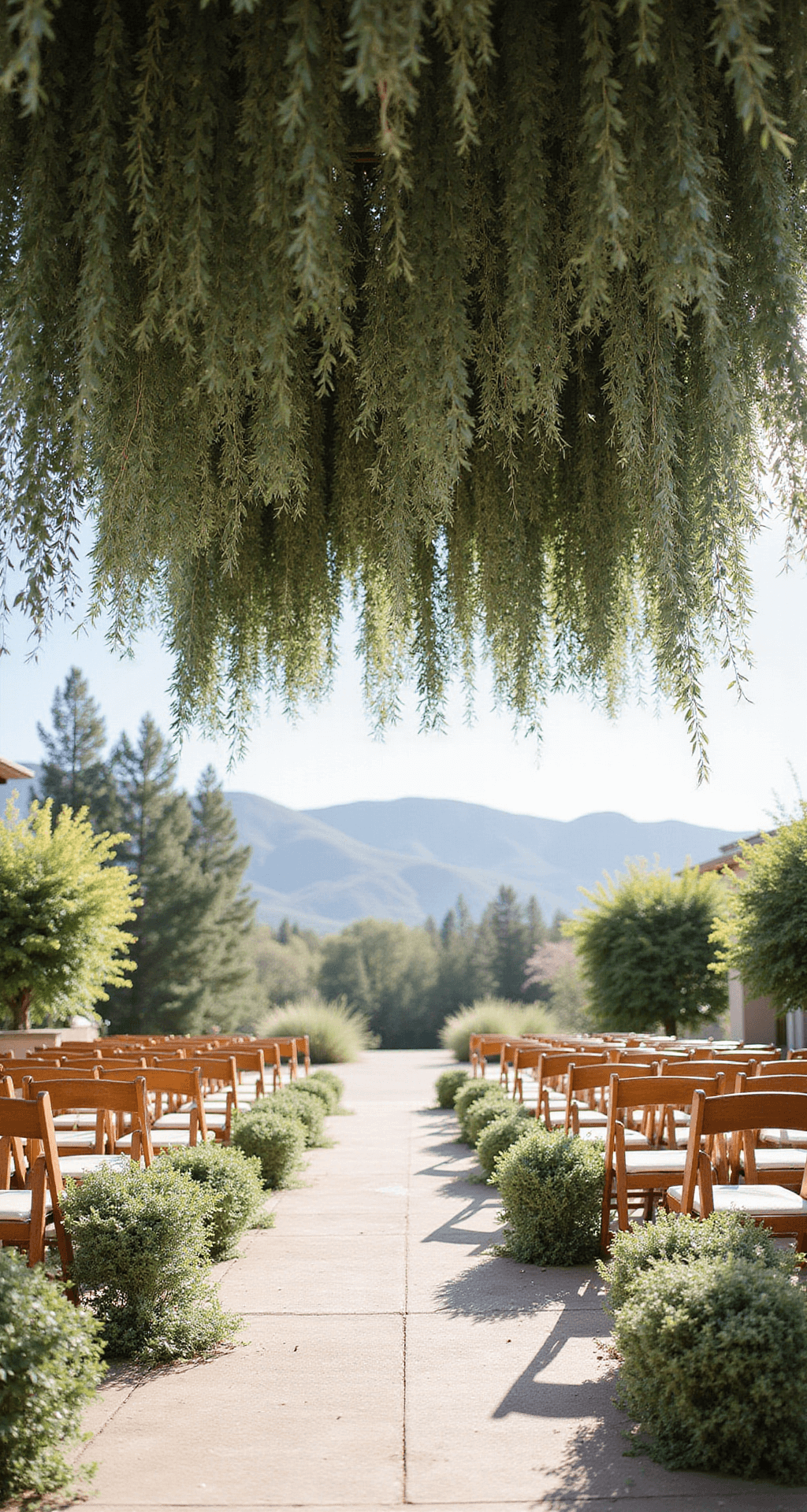 Wedding Ceremony Decorations: How to Design an Unforgettable Aisle and Backdrop A breathtaking outdoor ceremony space adorned with suspended garlands of eucalyptus and olive branches, bathed in soft sunlight, featuring wooden chairs with minimal fabric accents, set against a romantic garden backdrop with distant mountains, captured from an overhead perspective.