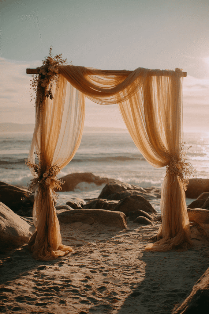 27 Luxury Wedding Arch Ideas for a Glamorous Ceremony Beachside wedding arch draped with soft flowing fabrics in natural tones, creating a romantic coastal ceremony backdrop with Pottery Barn-inspired light decor against sandy beach setting.