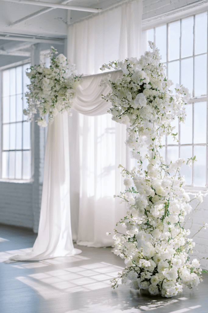 27 Luxury Wedding Arch Ideas for a Glamorous Ceremony Minimalist white floral arrangement with soft fabric draping and Crate and Barrel decor pieces on clean background